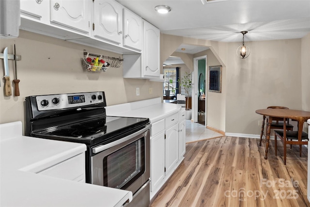 kitchen with light wood-style flooring, stainless steel electric range, arched walkways, light countertops, and white cabinetry