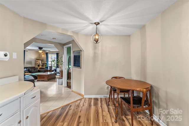 dining area featuring ceiling fan with notable chandelier, baseboards, arched walkways, and light wood-type flooring