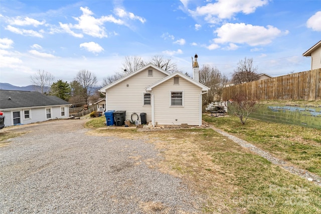 back of house with driveway, a chimney, and fence