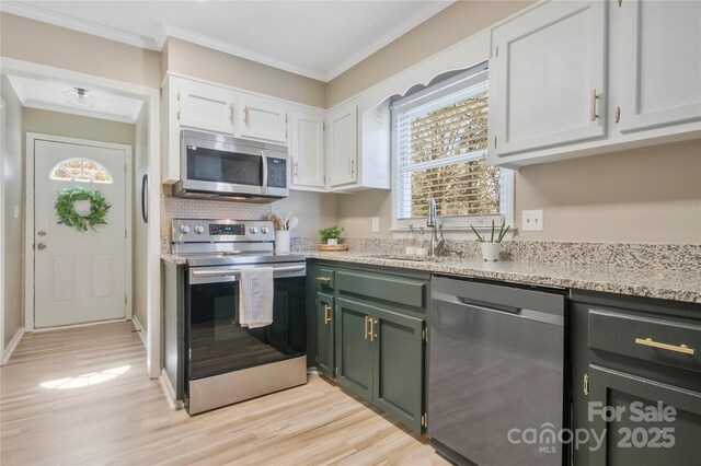 kitchen featuring light wood finished floors, white cabinets, stainless steel appliances, crown molding, and a sink