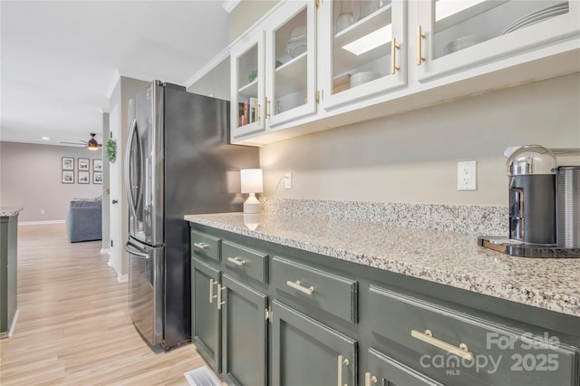 kitchen with visible vents, ceiling fan, glass insert cabinets, light stone counters, and light wood-style floors