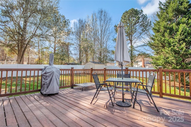 deck featuring outdoor dining space, fence, an outbuilding, and a shed