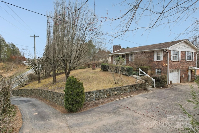 exterior space with a garage, driveway, brick siding, and a chimney