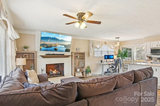 living area with a ceiling fan, a brick fireplace, and wood finished floors