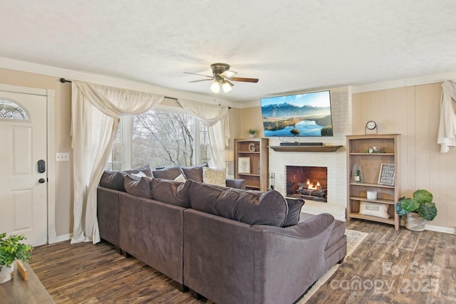 living area with a textured ceiling, dark wood-type flooring, a fireplace, a ceiling fan, and baseboards