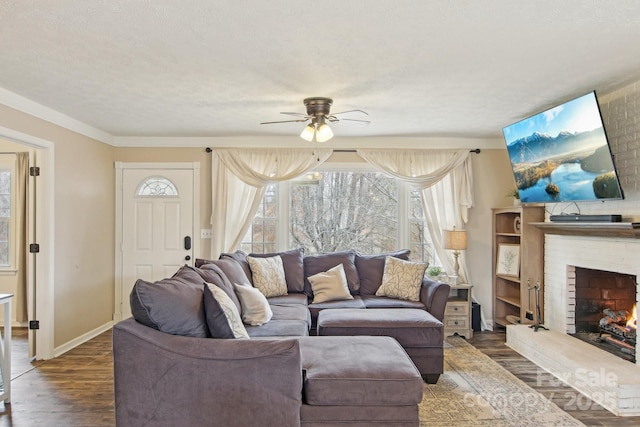 living area featuring baseboards, ceiling fan, wood finished floors, a textured ceiling, and a brick fireplace