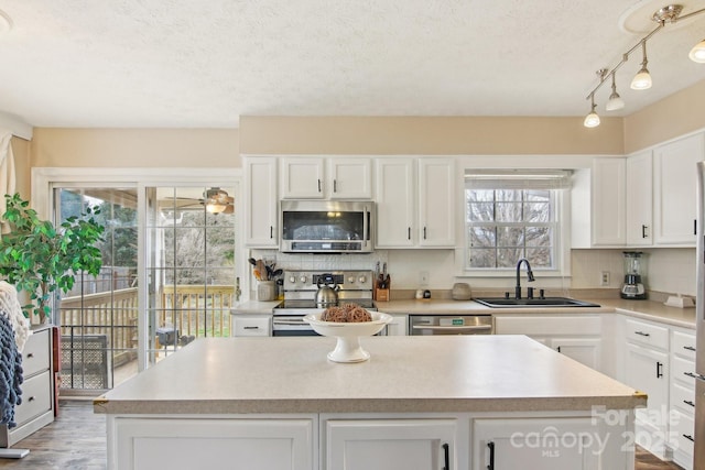 kitchen with white cabinets, a kitchen island, appliances with stainless steel finishes, a sink, and backsplash