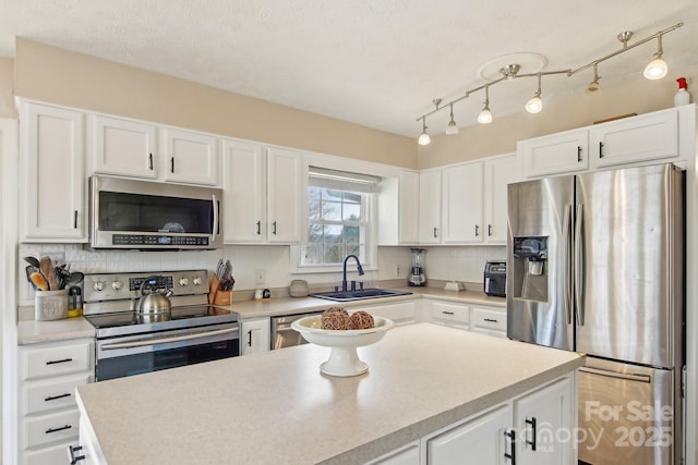 kitchen featuring light countertops, appliances with stainless steel finishes, white cabinets, a sink, and a kitchen island