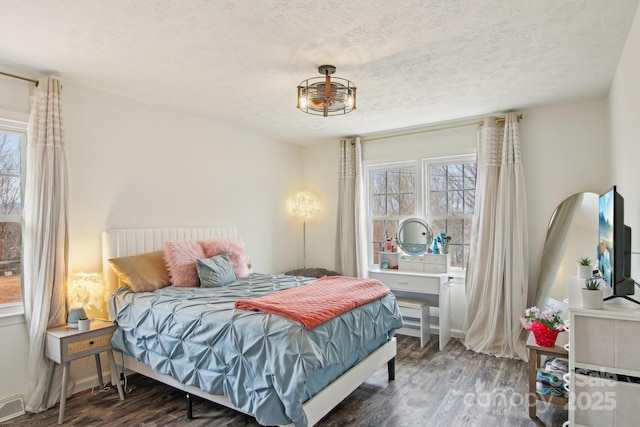 bedroom with visible vents, a textured ceiling, baseboards, and wood finished floors