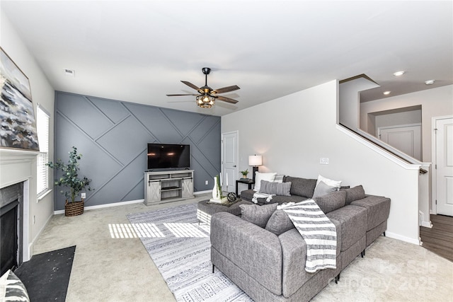 carpeted living room featuring an accent wall, baseboards, a high end fireplace, and ceiling fan