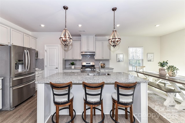 kitchen with a breakfast bar area, dark wood-style floors, a sink, under cabinet range hood, and appliances with stainless steel finishes