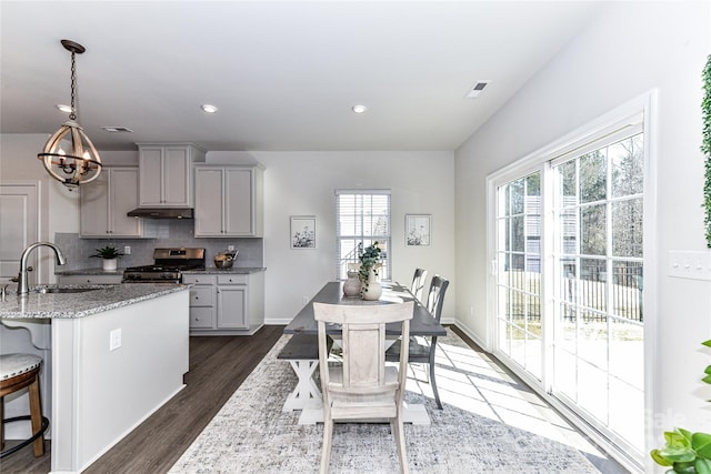 kitchen featuring a sink, backsplash, dark wood finished floors, light stone countertops, and stainless steel range with gas stovetop