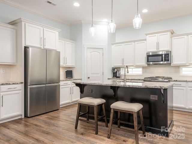 kitchen with ornamental molding, a sink, appliances with stainless steel finishes, white cabinetry, and a kitchen breakfast bar