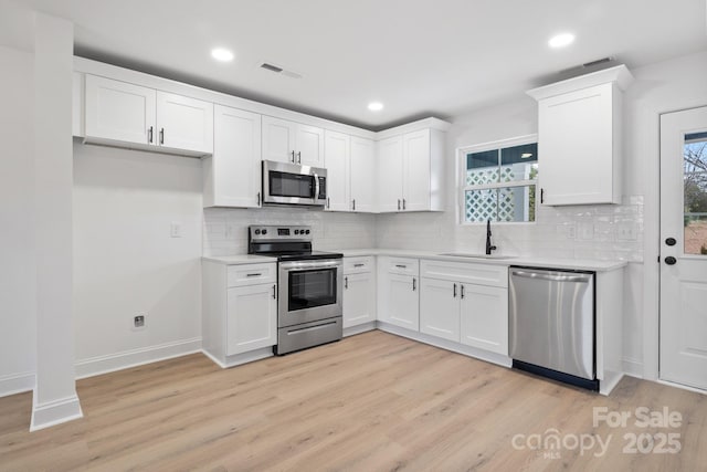 kitchen featuring light wood-type flooring, a sink, white cabinetry, appliances with stainless steel finishes, and light countertops