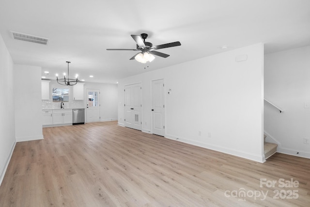 unfurnished living room with light wood-type flooring, visible vents, a sink, and stairway