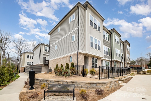 view of building exterior featuring central air condition unit, a residential view, and fence