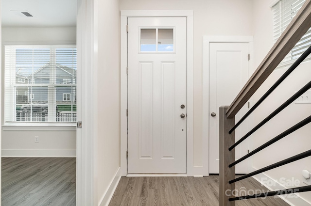 foyer entrance with light wood-style floors, stairs, baseboards, and a wealth of natural light