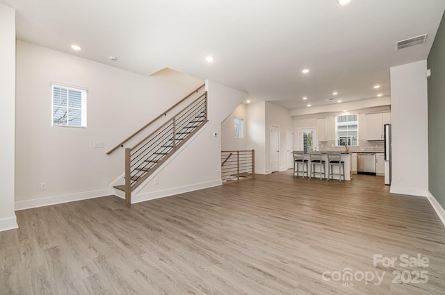 unfurnished living room featuring recessed lighting, visible vents, light wood-style flooring, and stairs