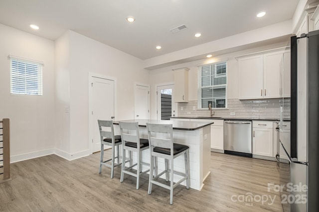 kitchen with light wood-style flooring, visible vents, appliances with stainless steel finishes, decorative backsplash, and a kitchen bar