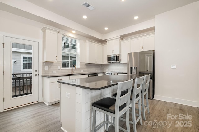 kitchen featuring appliances with stainless steel finishes, dark countertops, light wood-type flooring, and white cabinetry