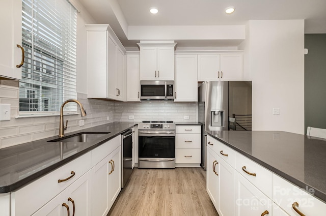 kitchen with a sink, stainless steel appliances, light wood-style floors, white cabinetry, and backsplash