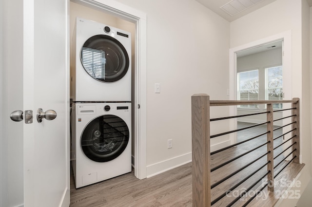 laundry area with stacked washer and dryer, visible vents, wood finished floors, laundry area, and baseboards