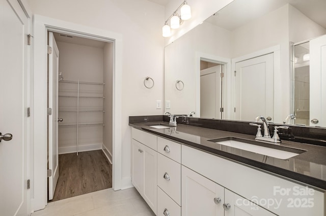 full bath featuring double vanity, a stall shower, a walk in closet, and a sink