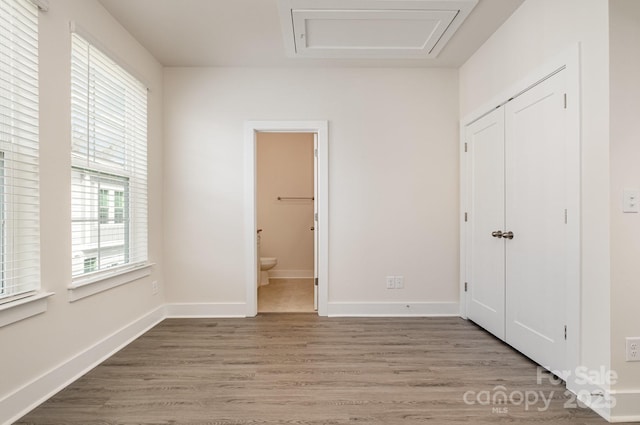 unfurnished bedroom featuring attic access, light wood-style floors, and baseboards