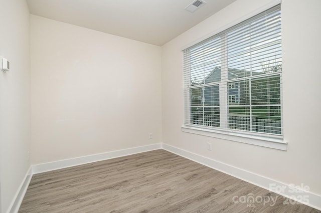 spare room with baseboards, visible vents, and wood finished floors