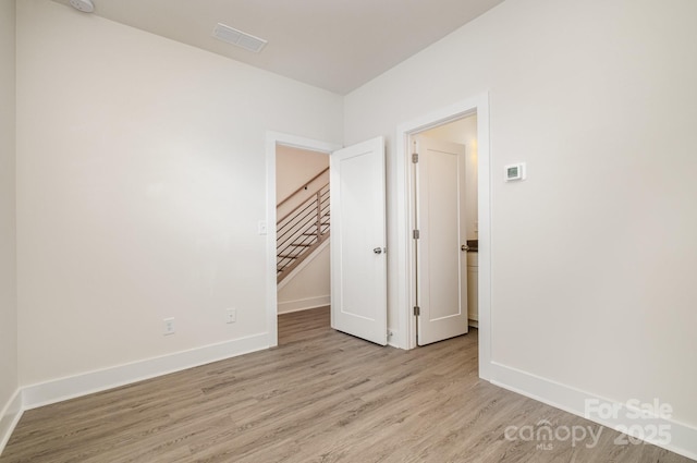 empty room featuring light wood finished floors, visible vents, stairs, and baseboards