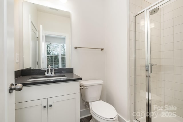 bathroom featuring toilet, visible vents, vanity, baseboards, and a stall shower