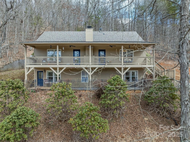 back of house with stairs, a ceiling fan, a shingled roof, and a chimney