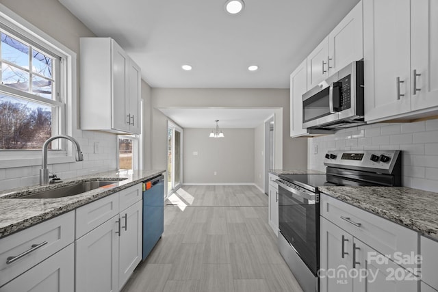 kitchen with stainless steel appliances, a sink, baseboards, white cabinets, and light stone countertops