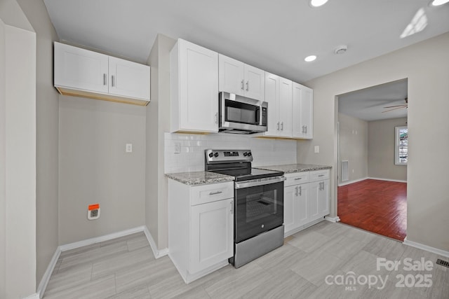 kitchen featuring light stone counters, stainless steel appliances, baseboards, white cabinets, and tasteful backsplash