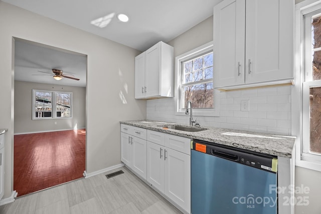 kitchen with a healthy amount of sunlight, a sink, dishwashing machine, and light stone countertops