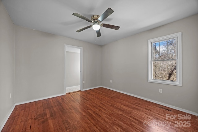 empty room featuring a ceiling fan, baseboards, visible vents, and wood finished floors