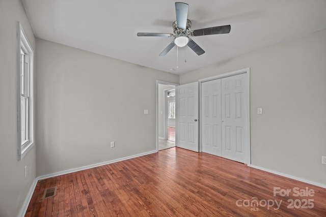 unfurnished bedroom featuring baseboards, multiple windows, visible vents, and wood finished floors