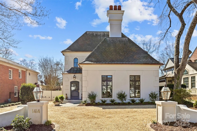 exterior space with metal roof, fence, stucco siding, a standing seam roof, and a chimney