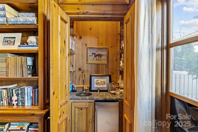 bar featuring freestanding refrigerator, wood walls, wet bar, and a sink