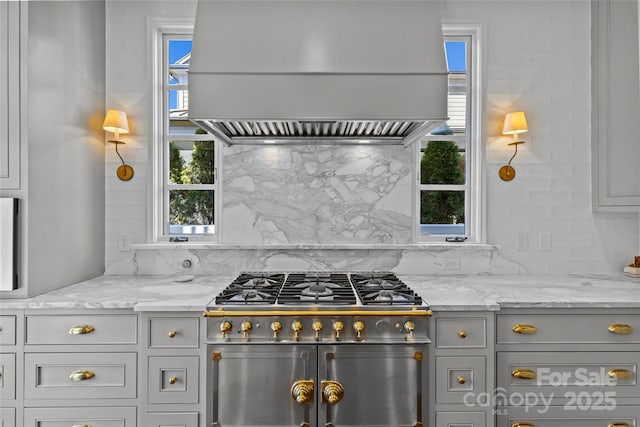 kitchen featuring range with two ovens, custom range hood, backsplash, gray cabinetry, and light stone countertops