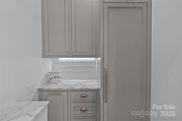 kitchen with light stone countertops, backsplash, and gray cabinetry