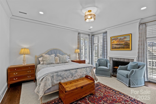 bedroom featuring visible vents, a tiled fireplace, wood finished floors, crown molding, and recessed lighting