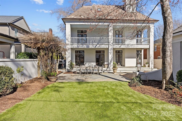 rear view of property featuring stucco siding, a patio, a balcony, and a lawn