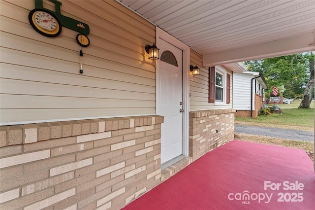 entrance to property featuring a porch and brick siding