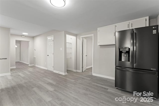 kitchen with light wood-style floors, white cabinets, baseboards, and black fridge