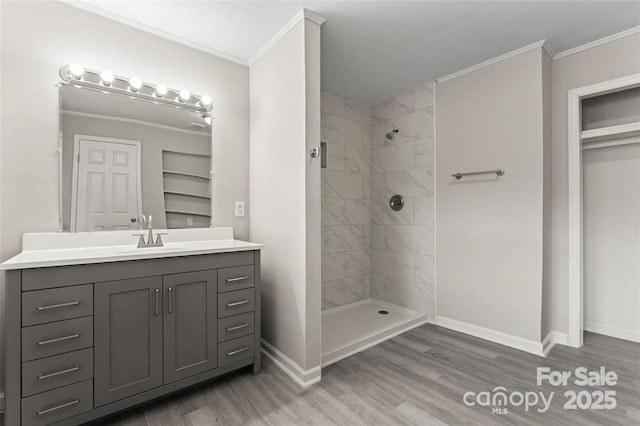 bathroom with ornamental molding, tiled shower, baseboards, and wood finished floors