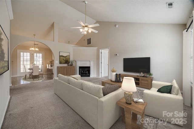 carpeted living room with a fireplace, visible vents, arched walkways, and high vaulted ceiling