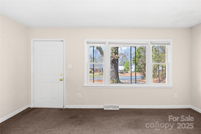 unfurnished room with dark colored carpet, visible vents, and baseboards