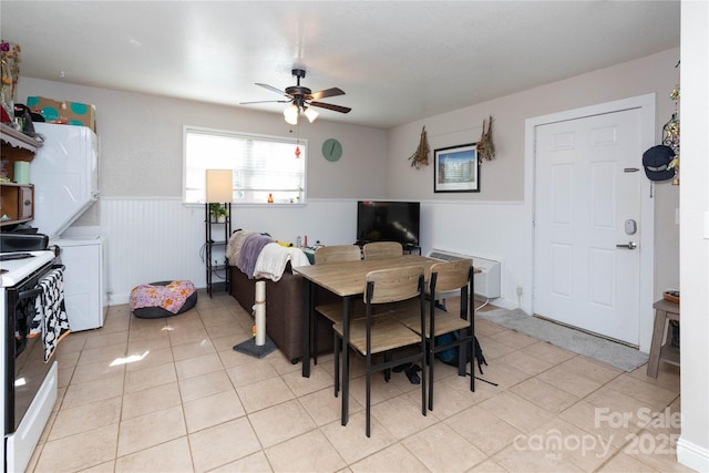 dining area with a ceiling fan, a wainscoted wall, stacked washing maching and dryer, and light tile patterned floors