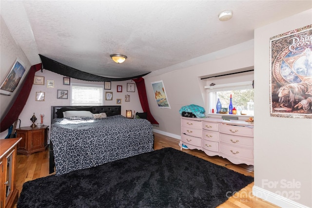 bedroom with a textured ceiling, light wood-style flooring, and baseboards